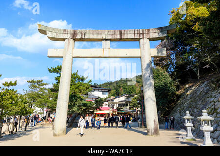 Giappone, Miyajima. Calcestruzzo Torii gate tra il terminal del traghetto e il Tempio di Itsukushima sul lungomare. Lo sfondo dello shopping, i turisti a piedi. Foto Stock