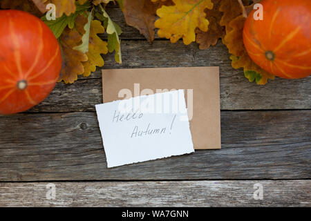Autunno flatlay composizione con lettera, busta craft, carta carta con testo scritto Ciao Autunno, foglie, zucche su vintage sfondo di legno. Appartamento Foto Stock
