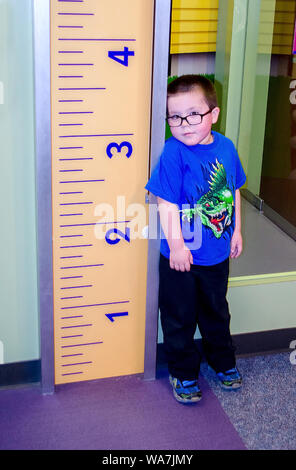 Un grazioso piccolo ragazzo sorge accanto a un gigantesco righello per vedere come alto egli è. Foto Stock