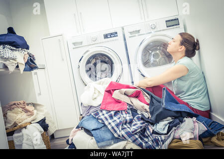 Stanco donna infelice casalinga in una sala lavanderia vicino alla macchina di lavaggio Foto Stock