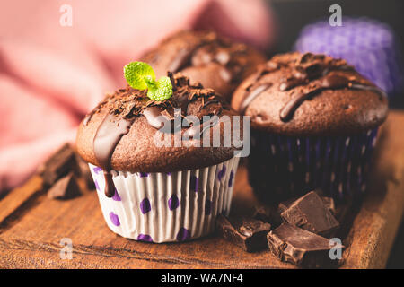 Muffin al cioccolato decorato con salsa di cioccolato e foglia di menta, servita sulla tavola di legno. Vista ingrandita, tonica immagine Foto Stock