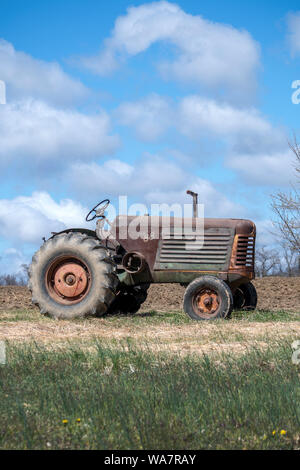 Aprile 28 2018 Buchanan MI USA; molto vecchio trattore seduti sulla cima di una collina con un nuovo campo arato Foto Stock