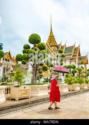 Bangkok, Thailandia - Giugno 2019: Donna asiatica non identificata in rosso, con un ombrello, visitando il Palazzo reale Foto Stock