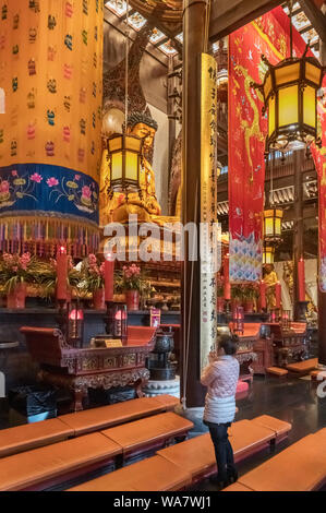 Donna orante davanti una statua del Buddha d'oro nella Grand Hall, il Tempio del Buddha di Giada, Shanghai, Cina Foto Stock