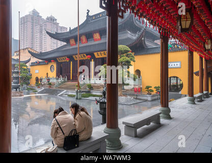 Due giovani donne si ripara dalla pioggia di fronte al Grand Hall presso il Tempio del Buddha di Giada, Shanghai, Cina Foto Stock