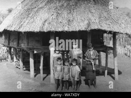 AJAXNETPHOTO. 1953-1957 (circa). INDO CINA. Il Vietnam. (IN POSIZIONE paese sconosciuto.) - ragazze, uno di fumare un bambù tradizionale tubo di acqua, e i ragazzi pongono per la fotocamera al di fuori del tetto di paglia HOUSE (HOOCH) su palafitte. foto:JEAN CORRÈZE/AJAXREF:RX7 191508 243 Foto Stock