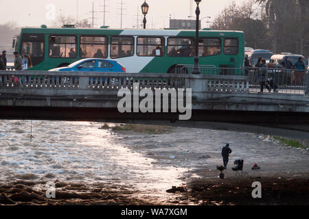 Pedoni e il traffico sul ponte sopra il fiume Mapocho, con uomo senza tetto sotto a Santiago del Cile Foto Stock