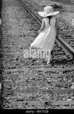 In bianco e nero di una bambina in un floppy hat e white sundress camminando lungo una ferrovia via Foto Stock