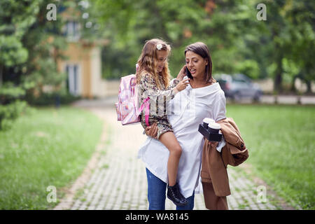 Occupato giovane mamma a piedi con sua figlia dopo la scuola Foto Stock