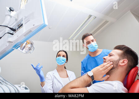 Ritratto di un bel giovane paziente di dolore con il dentista e il suo assistente. Foto Stock