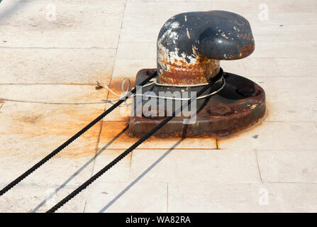 Grande vecchio arrugginito bollard con una corda di nero su un molo di pietra Foto Stock