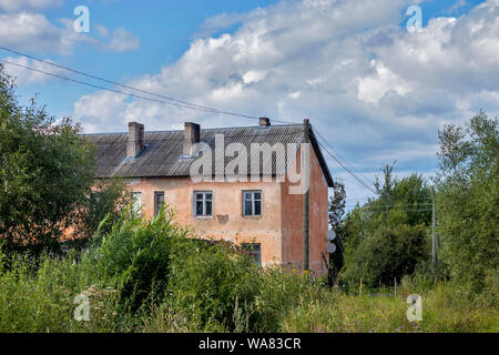 RUSSIA, DEMYANSK - Agosto 16, 2019, il vecchio abbandonato casa a 2 piani ricoperta con alberi Foto Stock