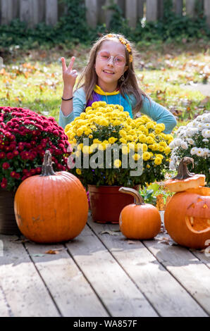 Una bambina vestita come un fiore hippie bambino, lampeggia un segno di pace come lei pone in costume di Halloween Foto Stock