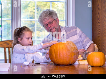 Il nonno guarda come un bambino disegna una faccia su una zucca per lui a scolpire Foto Stock