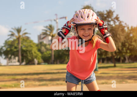 Bambina in casco e pattini a rotelle presso un parco all'aperto per bambini Foto Stock