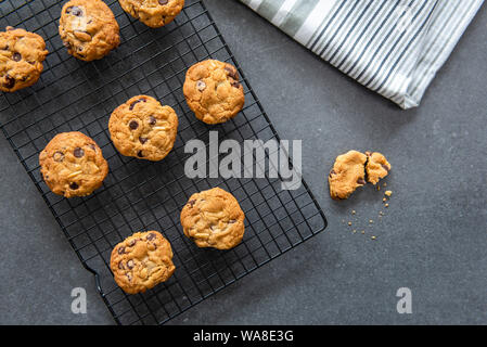 Pane appena sfornato in casa i biscotti al cioccolato con frutta e noci, mirtilli e mandorle, raffreddamento sul filo rack, sfondo scuro laici piatta Foto Stock