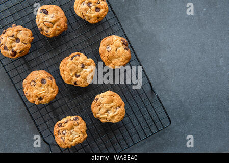 Pane appena sfornato in casa i biscotti al cioccolato con frutta e noci, mirtilli e mandorle, raffreddamento sul filo rack, sfondo scuro laici piatta Foto Stock