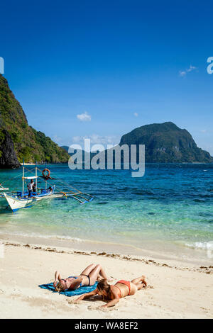 Turisti femmina a prendere il sole sulla spiaggia Pasandigan, El Nido, PALAWAN FILIPPINE Foto Stock