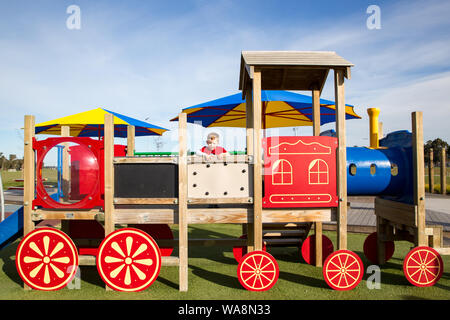 Un giovane bambino in età prescolare si arrampica sul colorato attività di legno treno in un parco pubblico in Nuova Zelanda Foto Stock