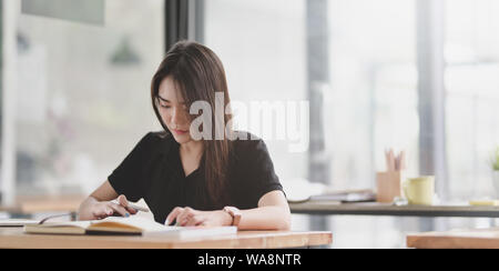 Attraente femmina giovane graphic designer di lettura e di lavoro per il suo progetto in moderno spazio di lavoro Foto Stock