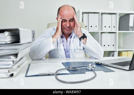 Triste frustrato coppia medico generale guardando aperta la cartella con i documenti e uno stetoscopio sulla sua scrivania Foto Stock