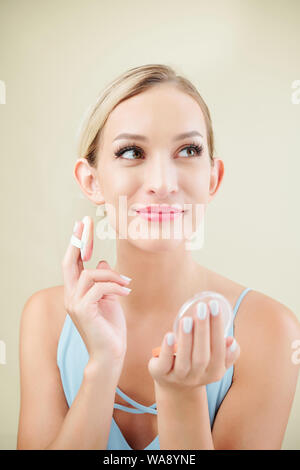 Ritratto di giovane sorridente donna caucasica applicando fondazione cuscino sul suo viso Foto Stock