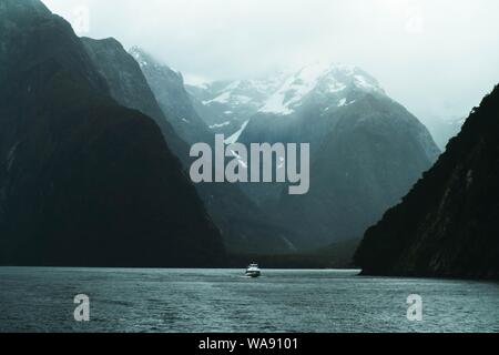 Beautiful shot of a lake with a cuddy boat sailing in the middle and rocky mountains on both sides Foto Stock
