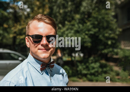 Ritratto di un bel giovane biondo con gli occhiali da sole in un parco della città. spazio copia Foto Stock