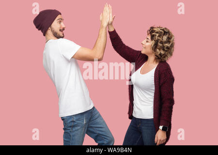 Vista laterale ritratto di felice coppia di amici in uno stile informale e permanente dando cinque per ogni altro con sorriso toothy, celebrando la vittoria. Isolato, Foto Stock