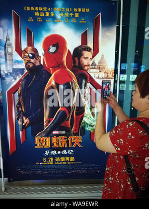 --FILE--un filmgoer attende di fronte un poster di American film del supereroe 'Uomo Ragno: lontano da casa in un cinema della città Yichang, centrale della Cina di Hube Foto Stock