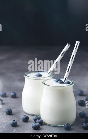 Lo yogurt greco con mirtilli in vasi di vetro con carta paglia su sfondo grigio. Una sana alimentazione e dieta concetto. Primo piano. Foto Stock