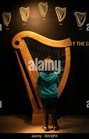 Irlanda turismo giovane ragazza turistica che gioca su una replica Guinness arpa irlandese nella Guinness Storehouse and Museum, Dublino, Irlanda Foto Stock