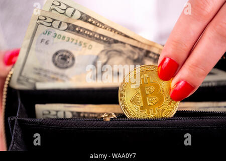 Virtual cryptocurrency denaro Bitcoin monete d'oro nella mano sinistra di una donna con il rosso smalto per unghie e un portamonete. Il futuro di denaro. Dollari USA. Foto Stock