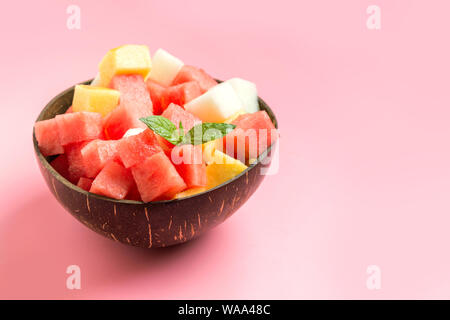 Una sana insalata di frutta di cocomero, melone e mango in tazza di cocco su sfondo rosa. Pulire mangiare cibo vegetariano concetto. Close up. Foto Stock