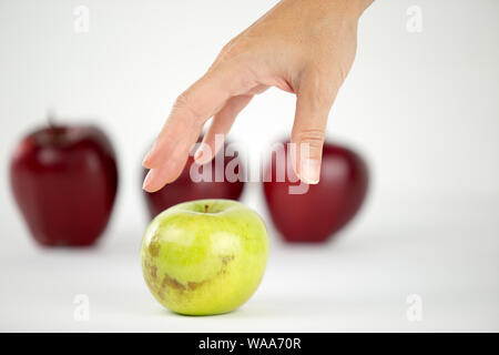 Concetto di diversità: una donna di mano è circa di agguantare il solo verde apple tra gli altri quelli rossi Foto Stock