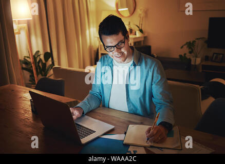 Uomo felice di lavorare da soli con un computer portatile aperto su una scrivania a casa Foto Stock