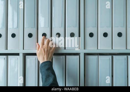Imprenditrice navigando attraverso il ring binder file archivio di documentazione sul ripiano in ufficio business, stretta di mano Foto Stock