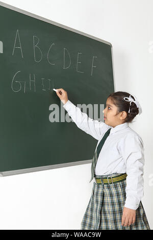 Schoolgirl writing alphabets on blackboard Stock Photo