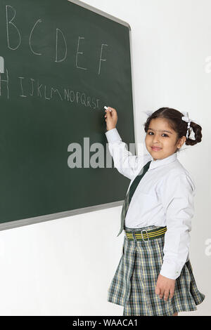 Schoolgirl writing alphabets on blackboard Stock Photo