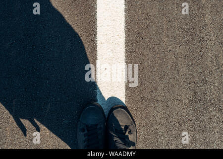 Esploratore urbano, uomo in scarpe moderne permanente sulla strada asfaltata con marcature bianche e spazio di copia Foto Stock