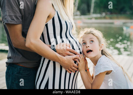 Immagine di uomo e ragazza abbracciando la donna incinta la pancia sul giorno di estate Foto Stock