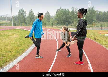 Un gruppo di giovani atleti interculturale facendo wam-up esercizi sulle piste Foto Stock