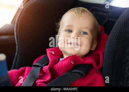 Carino toodler caucasica ragazzo seduto nel seggiolino di sicurezza in auto durante il viaggio. Adorable baby sorridente e godendo di viaggio nel luogo confortevole in Foto Stock