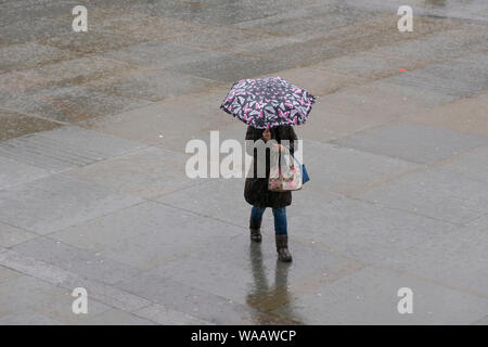 La gente camminare sotto la pioggia, Trafalgar Square, Londra, Gran Bretagna. Foto Stock