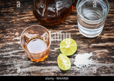 Bevande alcoliche e limone sale sul legno rustico background / brandy in un bicchiere con bottiglie di alcol e acqua - vodka rum tequila cognac e whisky co Foto Stock