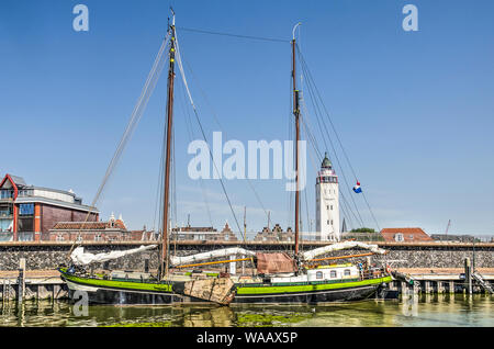 Harlingen, Paesi Bassi, 26 Luglio 2019: storica barca a vela ormeggiata a Nieuwe Willems del porto con la nuova difesa costiera parete e il faro Foto Stock