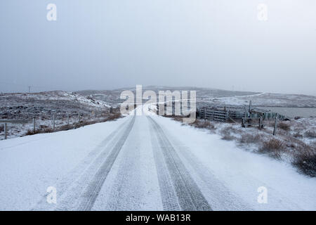 Una strada innevata in un ambiente rurale con deboli tracce di pneumatici e un fondale grigio con una stanza per la copia Foto Stock