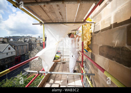 Colin Morris, da Nevin di pittori di Edimburgo, si applica la foglia di oro a uno dei royal stemmi durante i lavori di ristrutturazione sulla facciata principale di Canongate Kirk di Edimburgo. Foto Stock