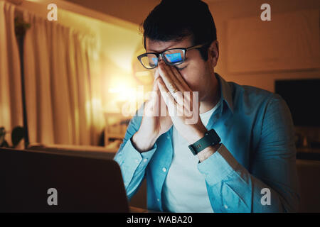 Uomo seduto nella sua stanza a lavorare fino a tarda notte con un senso molto stanca Foto Stock