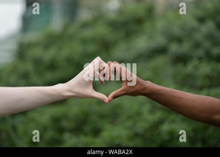 Luce e di carnagione scura uomini rendendo il cuore con le mani Foto Stock